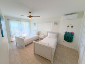 A bedroom with two beds, a ceiling fan, a window with blinds, and a wall-mounted air conditioner. - Sweeping Ocean & Koko Head Views - Ridgetop Home (Honolulu)