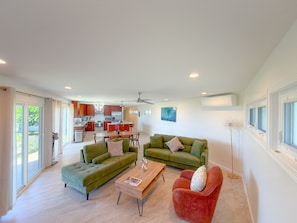 A spacious living area with a green sofa, a red armchair, and a wooden coffee table. A kitchen with modern appliances is visible in the background. - Sweeping Ocean & Koko Head Views - Ridgetop Home (Honolulu)