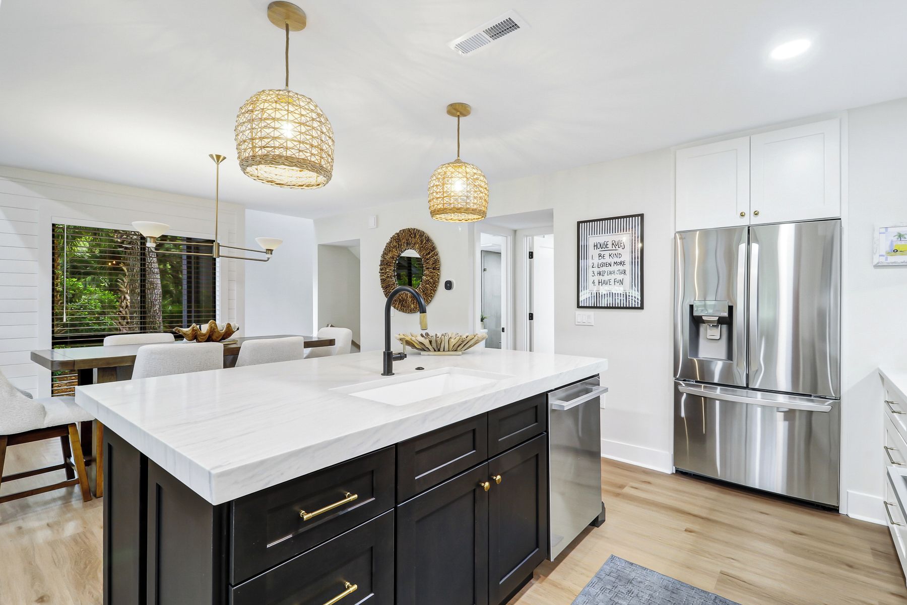 A modern kitchen with a marble countertop, black cabinetry, stainless steel appliances, and pendant lighting.