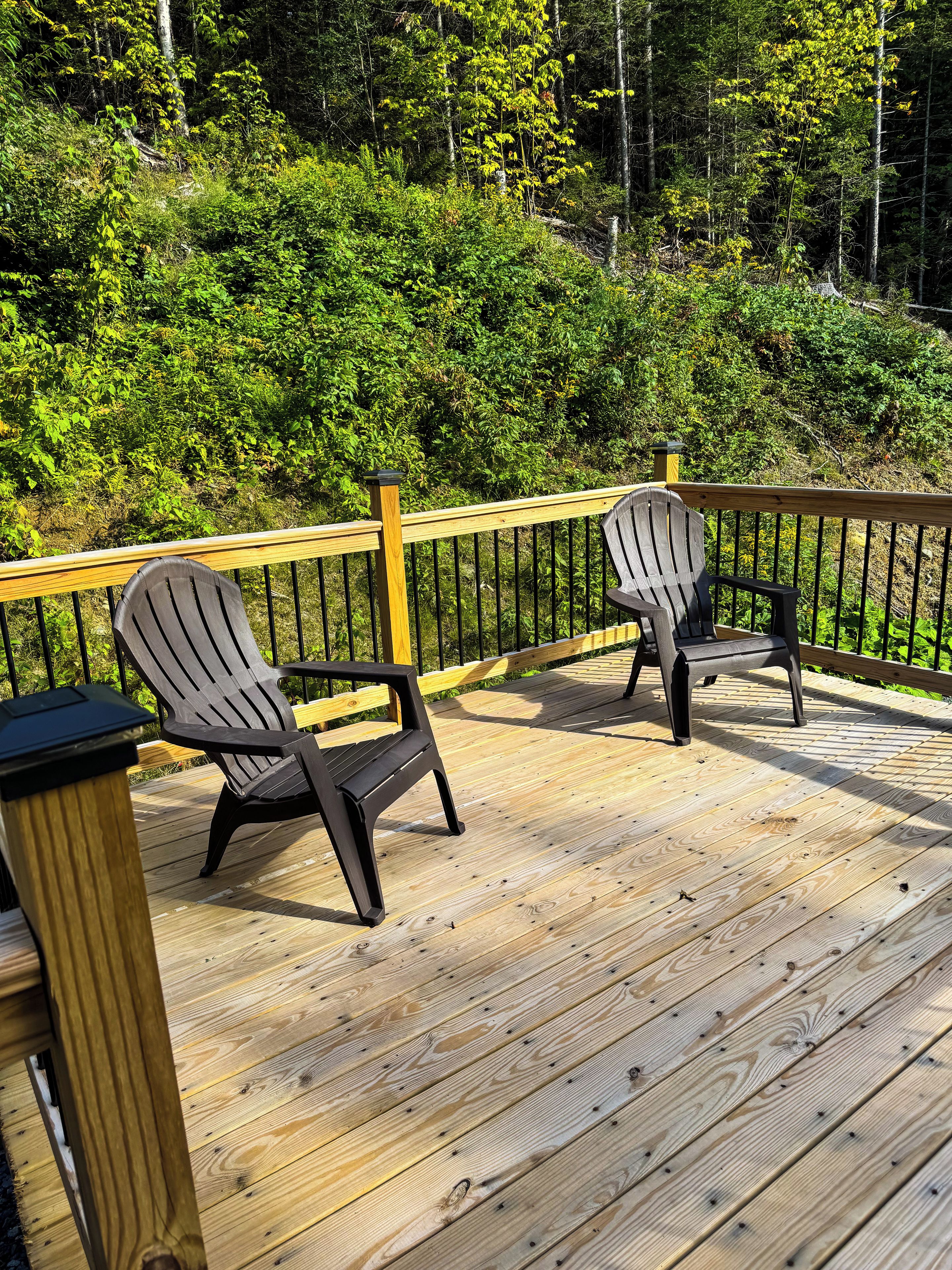 Una terraza de madera con dos sillas Adirondack y una barandilla de madera.