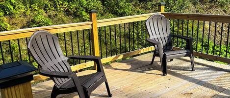 Una terraza de madera con dos sillas Adirondack y una barandilla de madera.