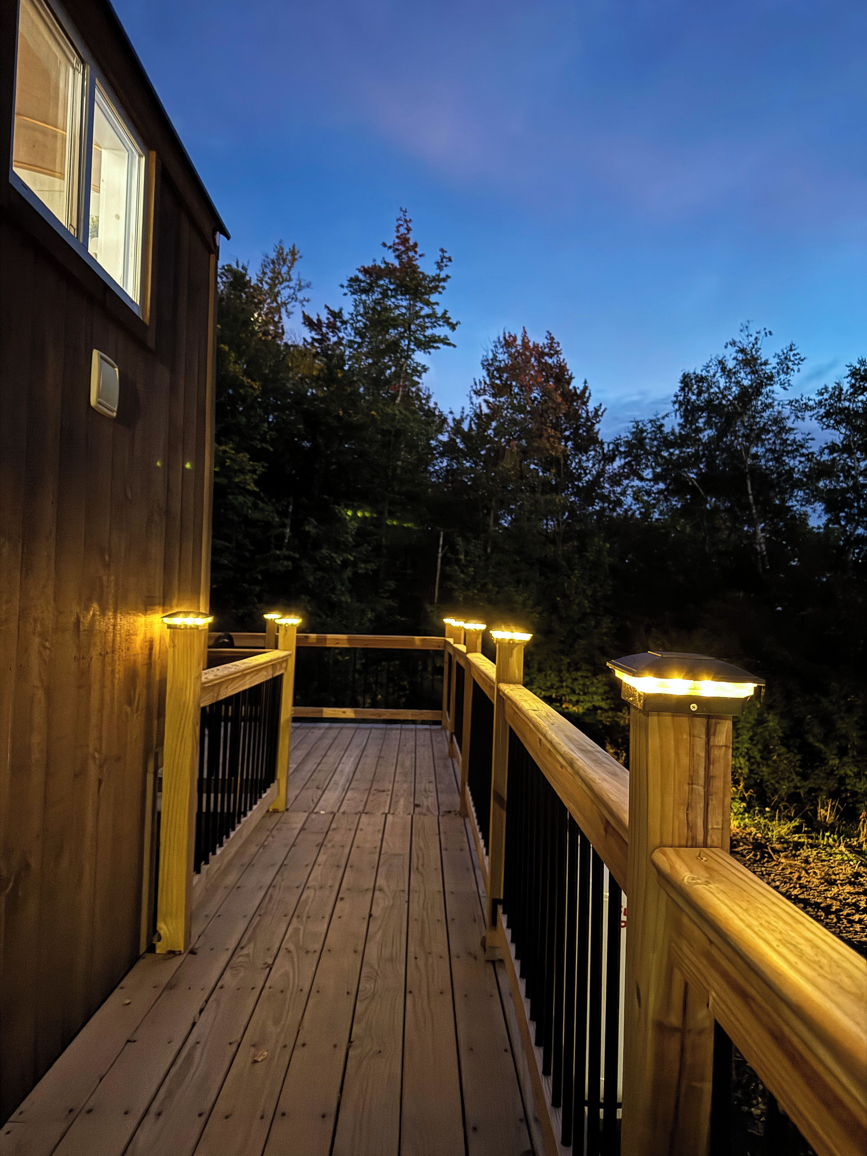 A wooden deck with railings and lights, leading to a building with windows.