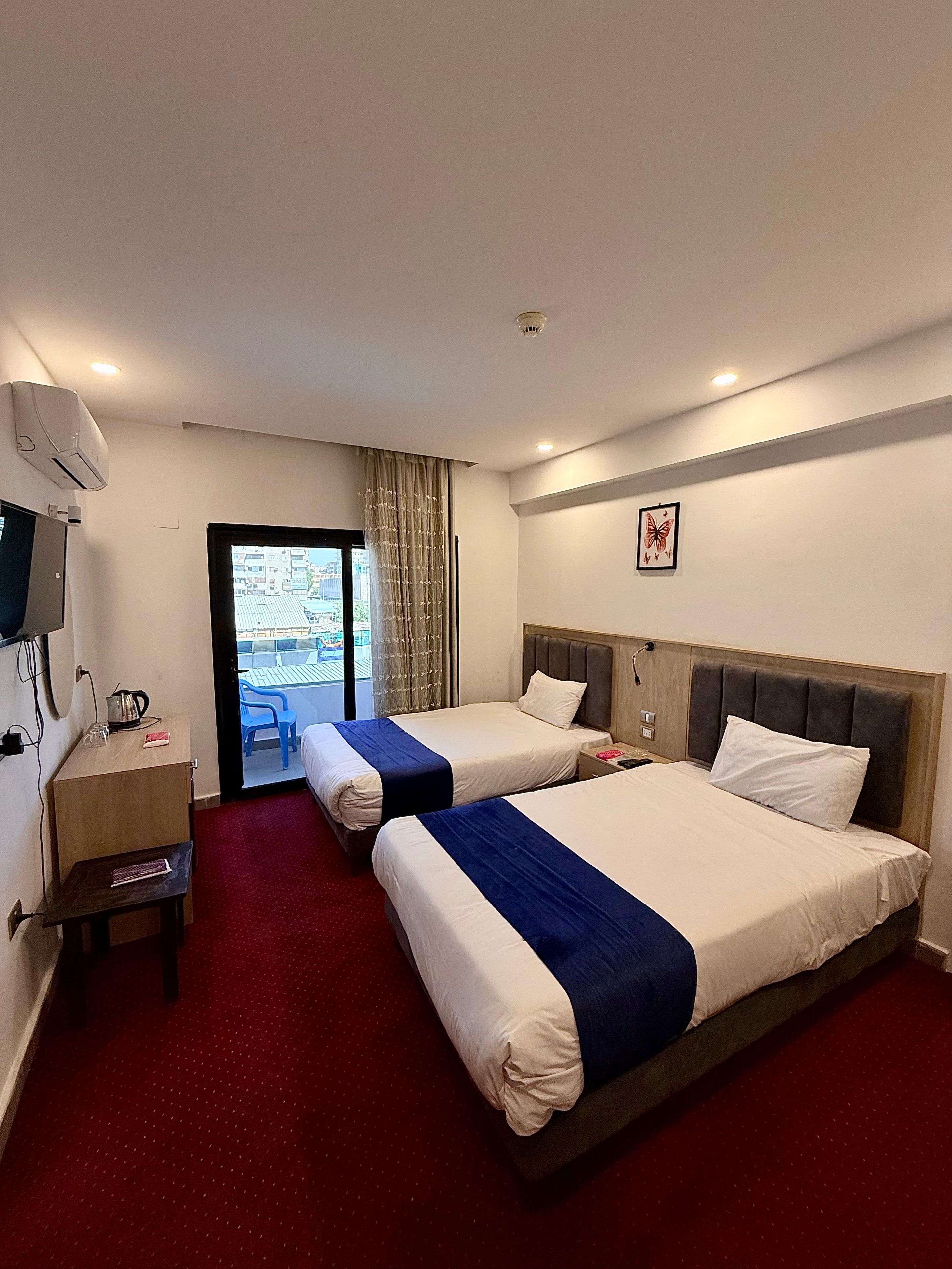 A hotel room with two beds, a desk, a TV, and a view of the city.