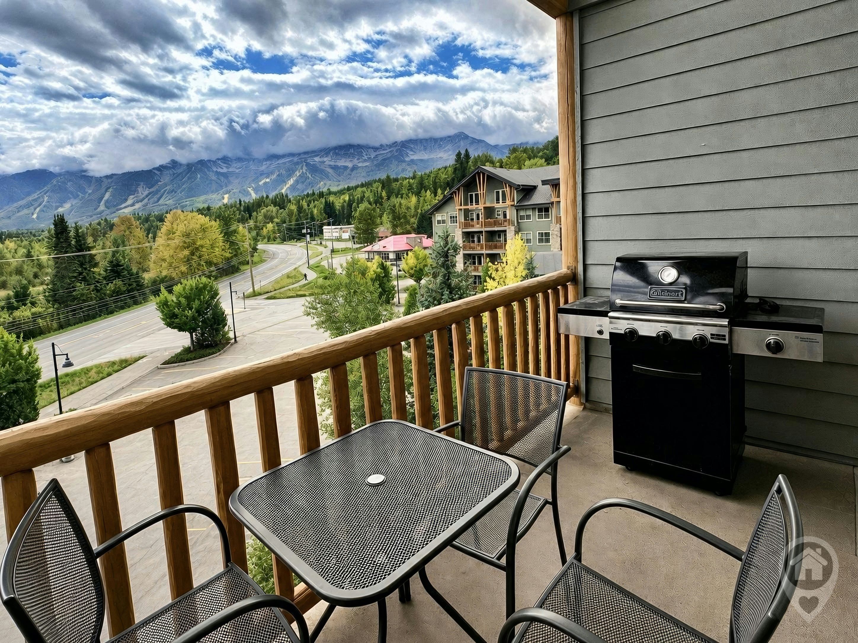 A balcony with a grill, chairs, and a view of mountains and buildings.