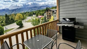 A balcony with a grill, chairs, and a view of mountains and buildings.