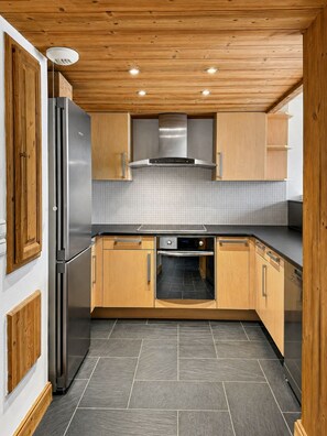 Eine moderne Küche mit Holzschränken, einem Edelstahlkühlschrank, einem eingebauten Backofen und einer gefliesten Spritzschutzwand.