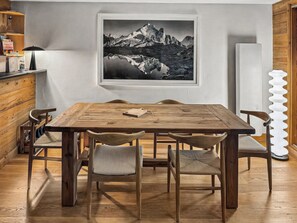 Ein Essbereich mit einem Holztisch und Stühlen, einem gerahmten Bild von einer Berglandschaft an der Wand und einem weißen Kühlschrank.
