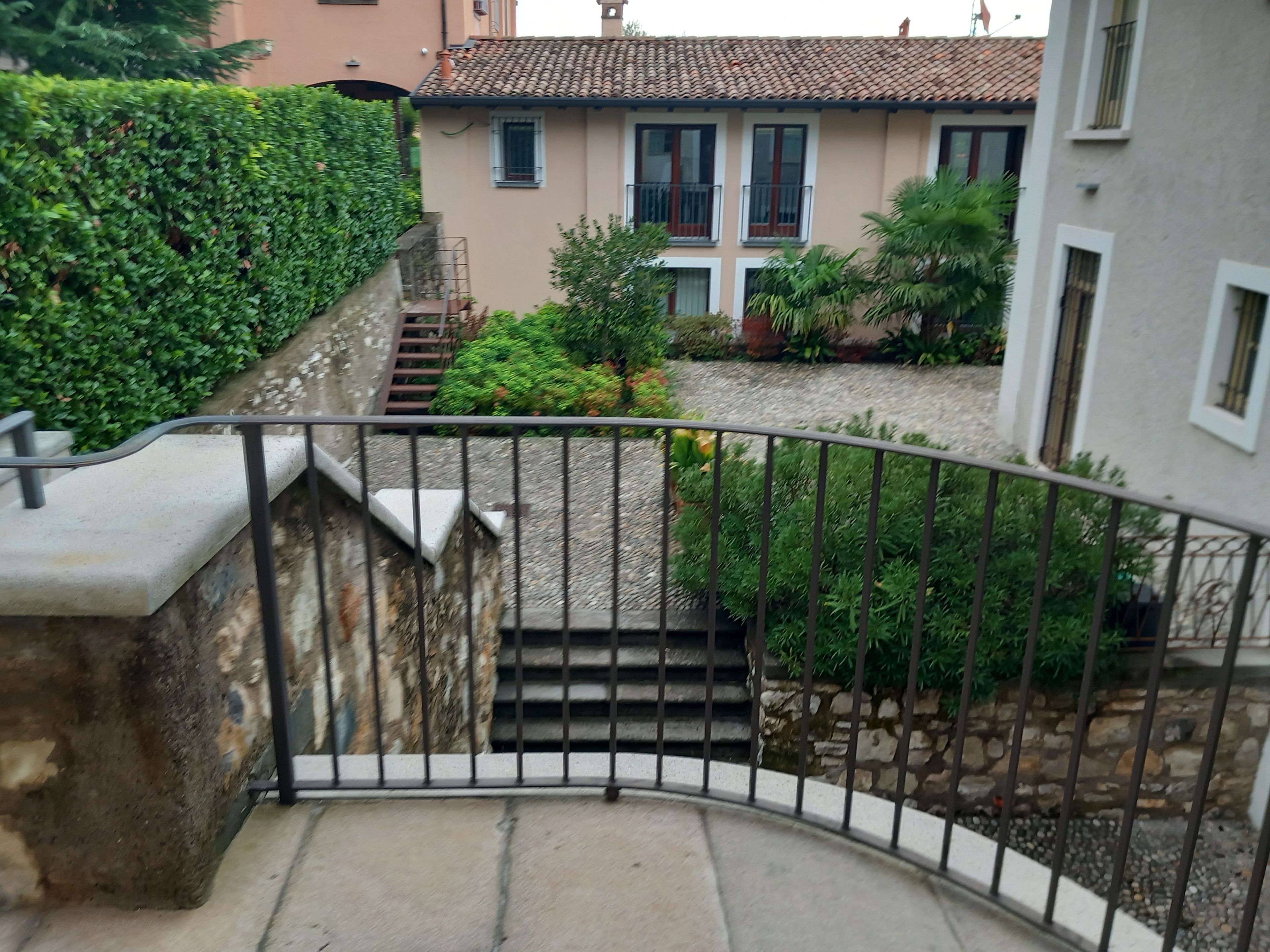 A curved staircase with a metal railing leading to a building with a tiled roof and windows.