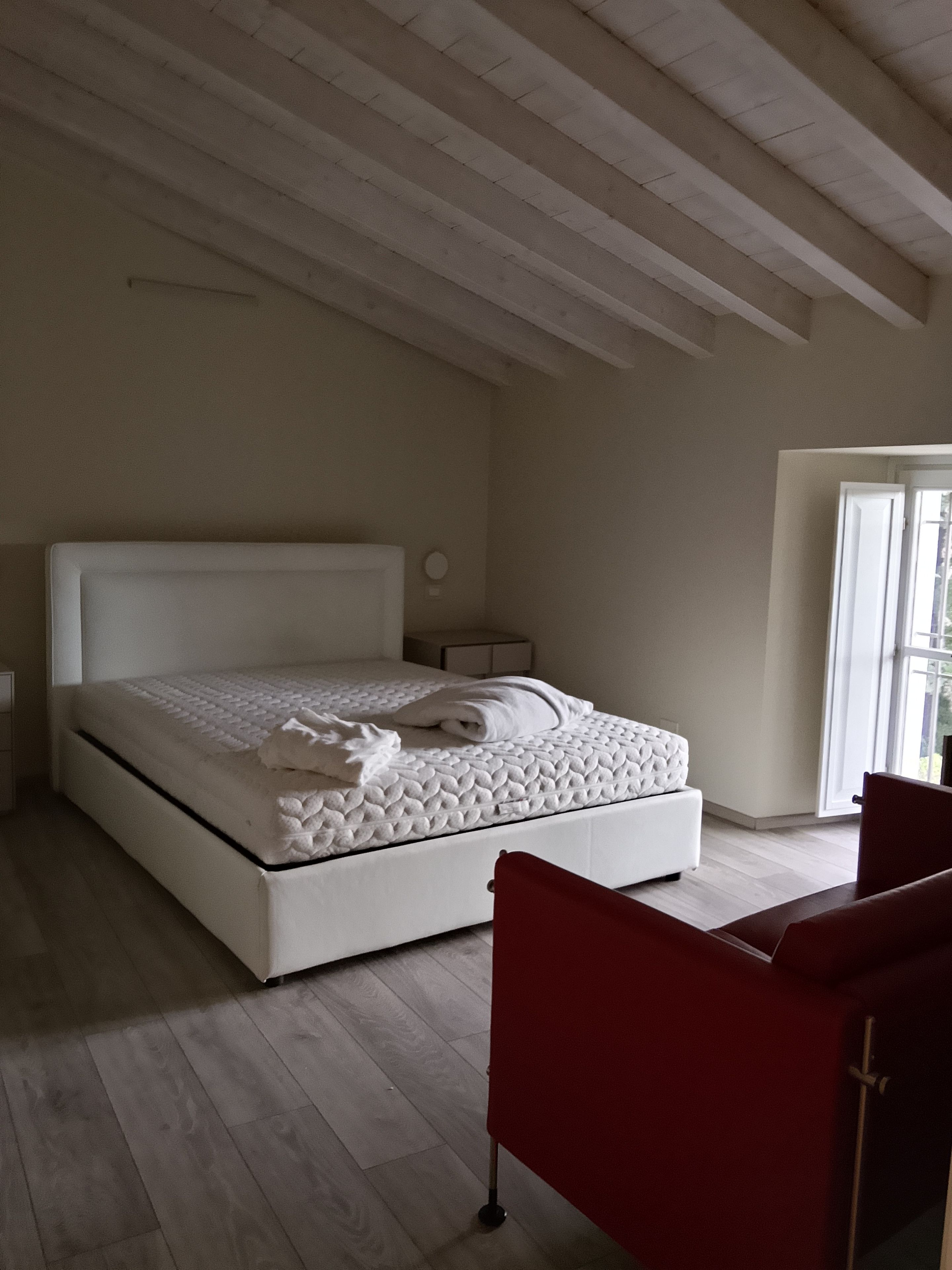A bedroom with a large bed, a red chair, and a window.