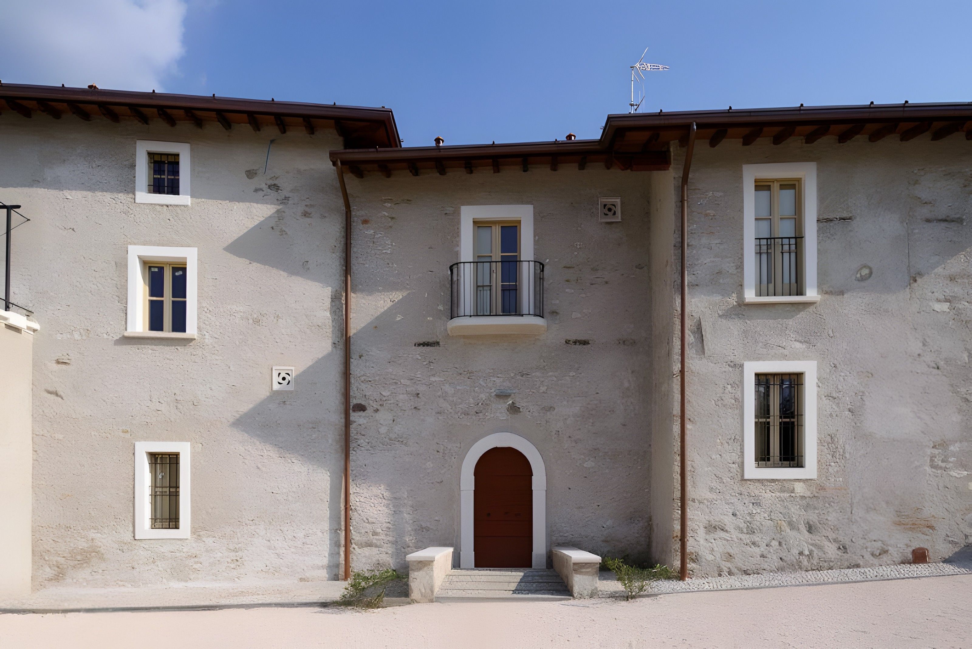A two-story building with a central entrance, a balcony on the second floor, and multiple windows.