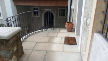 A curved balcony with a stone ledge, a metal railing, a potted plant, and a door with a doormat.