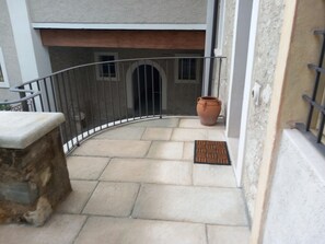 A curved balcony with a stone ledge, a metal railing, a potted plant, and a door with a doormat.