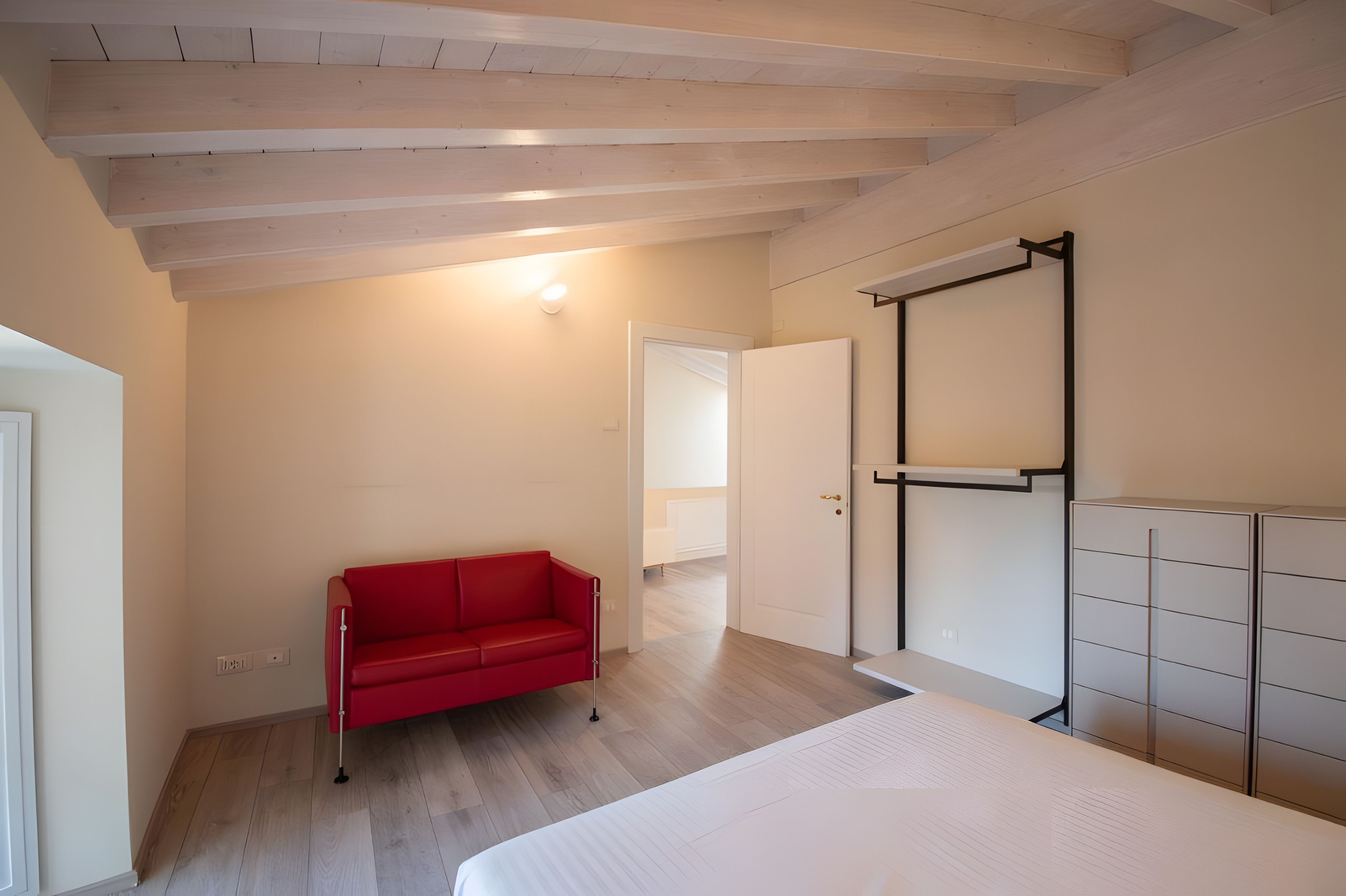 A room with a bed, a red sofa, a wardrobe, and a door leading to another room.