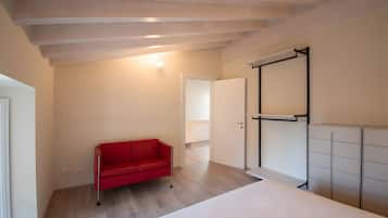 Una habitación con cama, sofá rojo, armario y puerta que da a otra estancia.