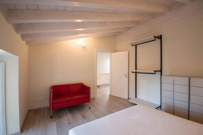 Una habitación con cama, sofá rojo, armario y puerta que da a otra estancia.