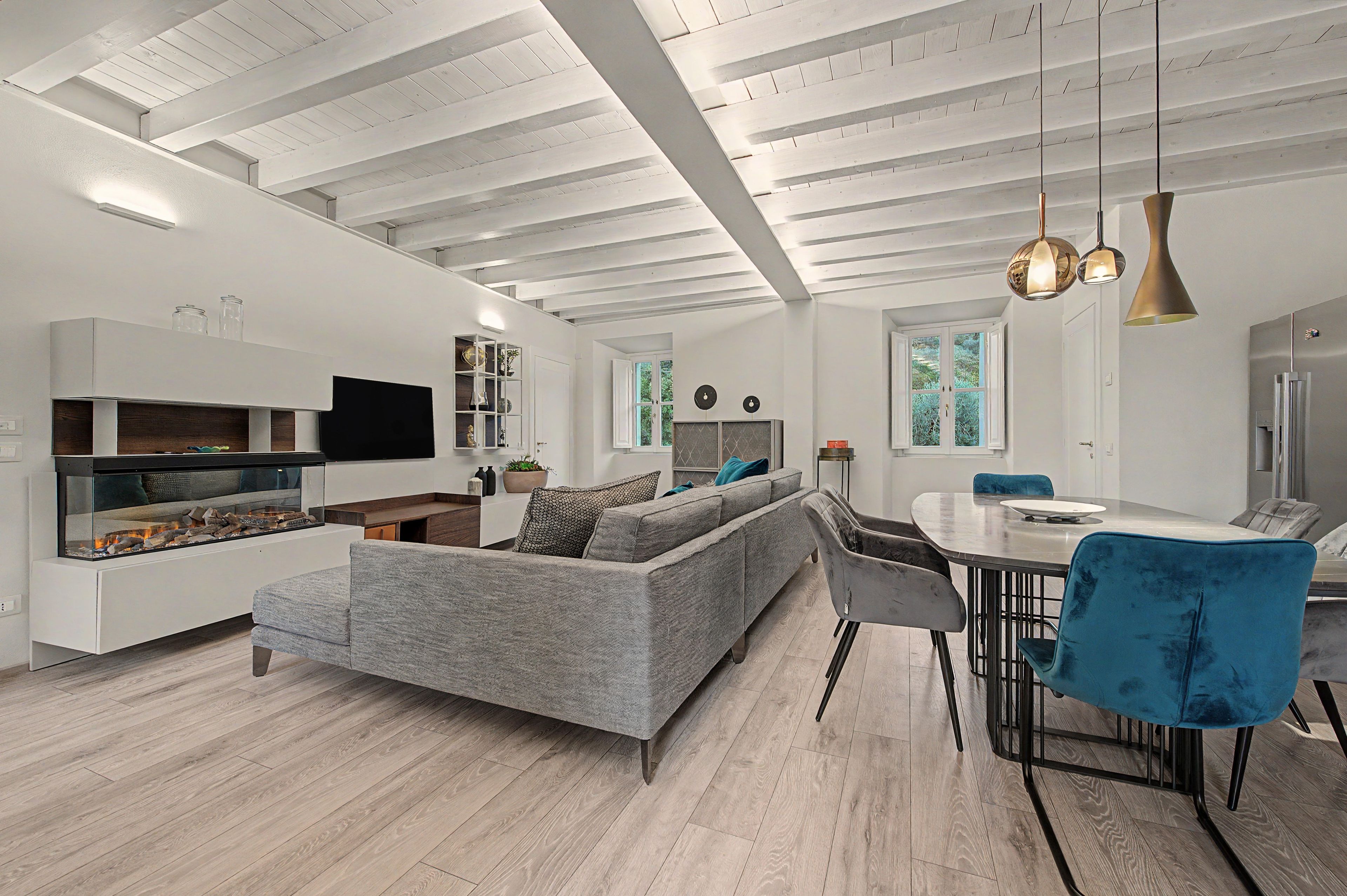 A modern living room with a built-in fireplace, grey sofa, dining table with chairs, and pendant lighting.