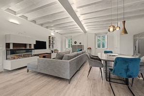 A modern living room with a built-in fireplace, grey sofa, dining table with chairs, and pendant lighting.