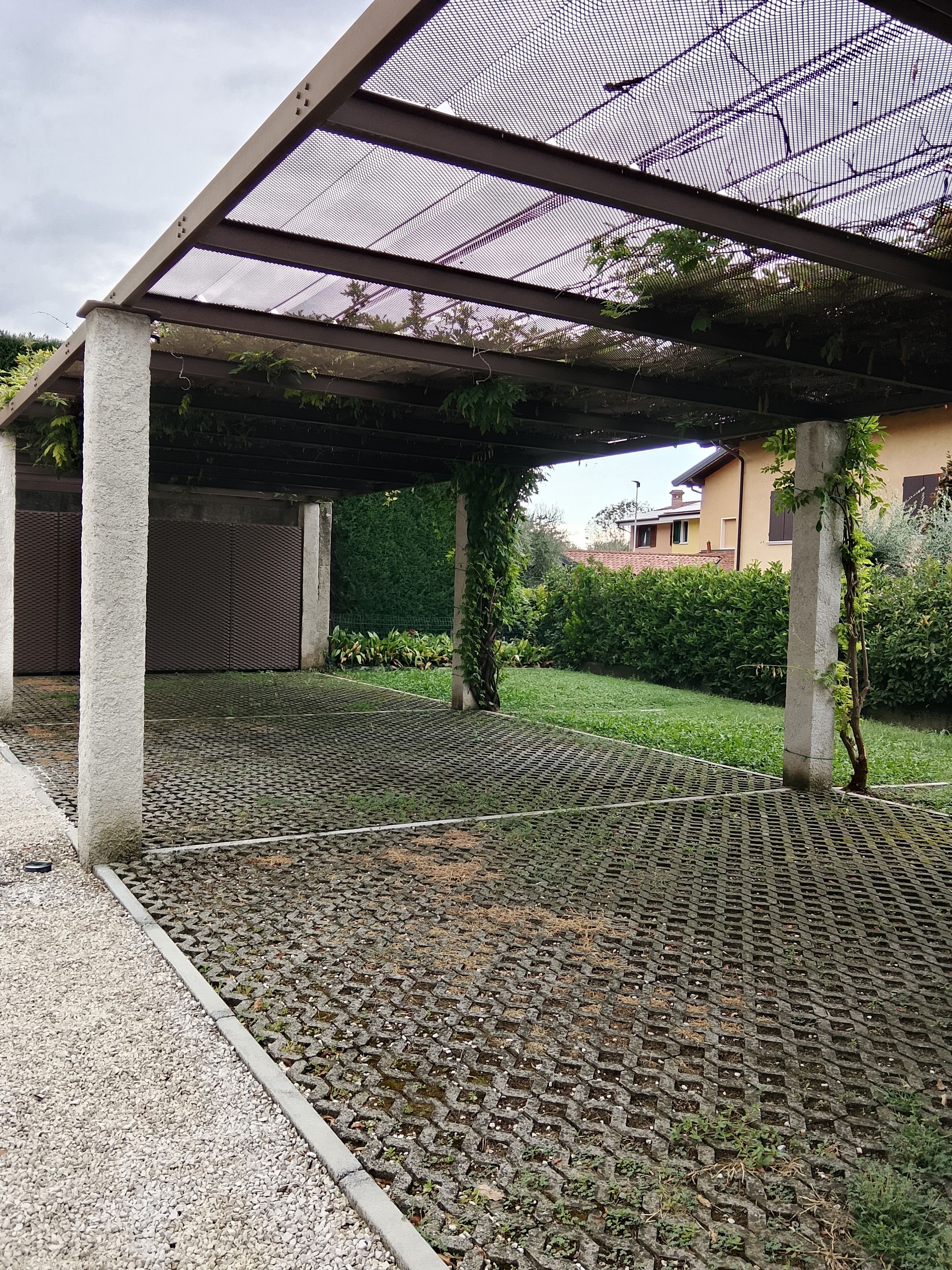 A covered outdoor area with a patterned floor, concrete pillars, and a mesh roof.
