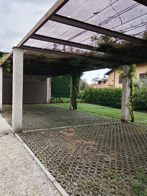 Un espacio al aire libre techado con suelo estampado, pilares de hormigón y techo de malla.