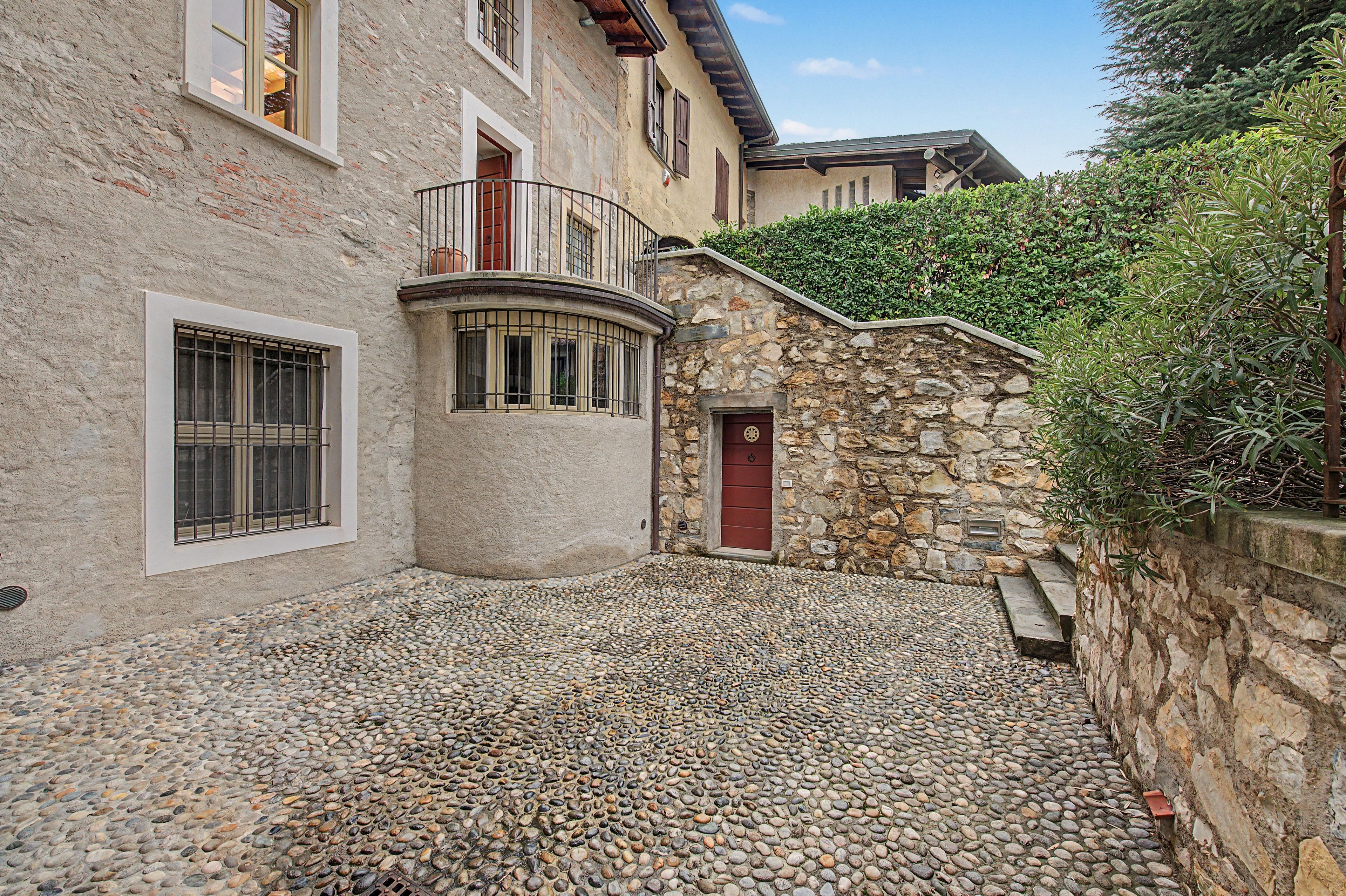 Ein Innenhof mit einer Steinmauer, einer roten Tür und einem Balkon mit Metallgeländern.