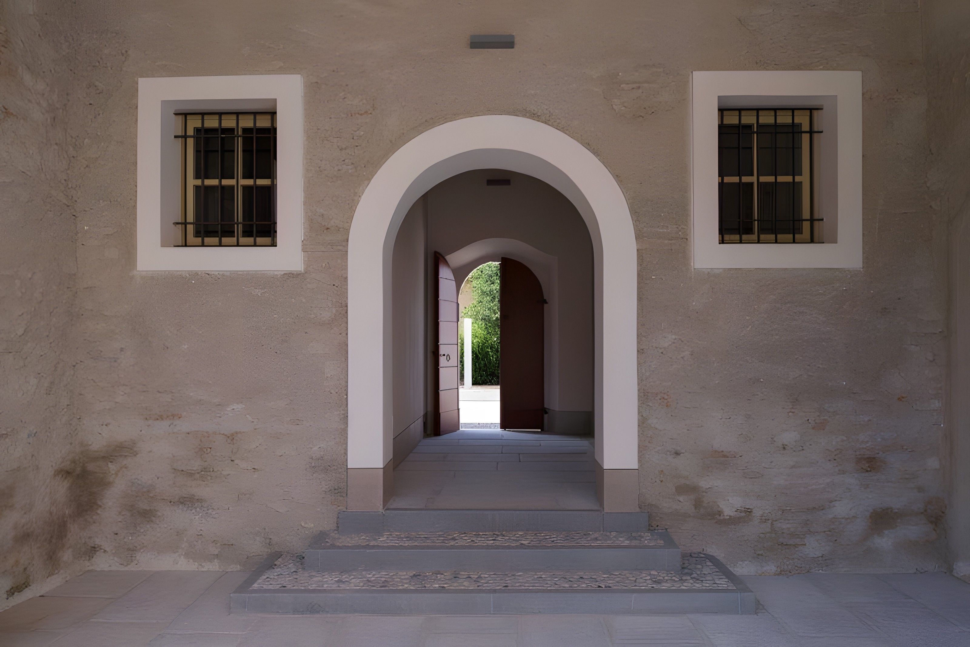 Un couloir doté d’une entrée en arc, flanqué de deux fenêtres ornées de motifs à barreaux.