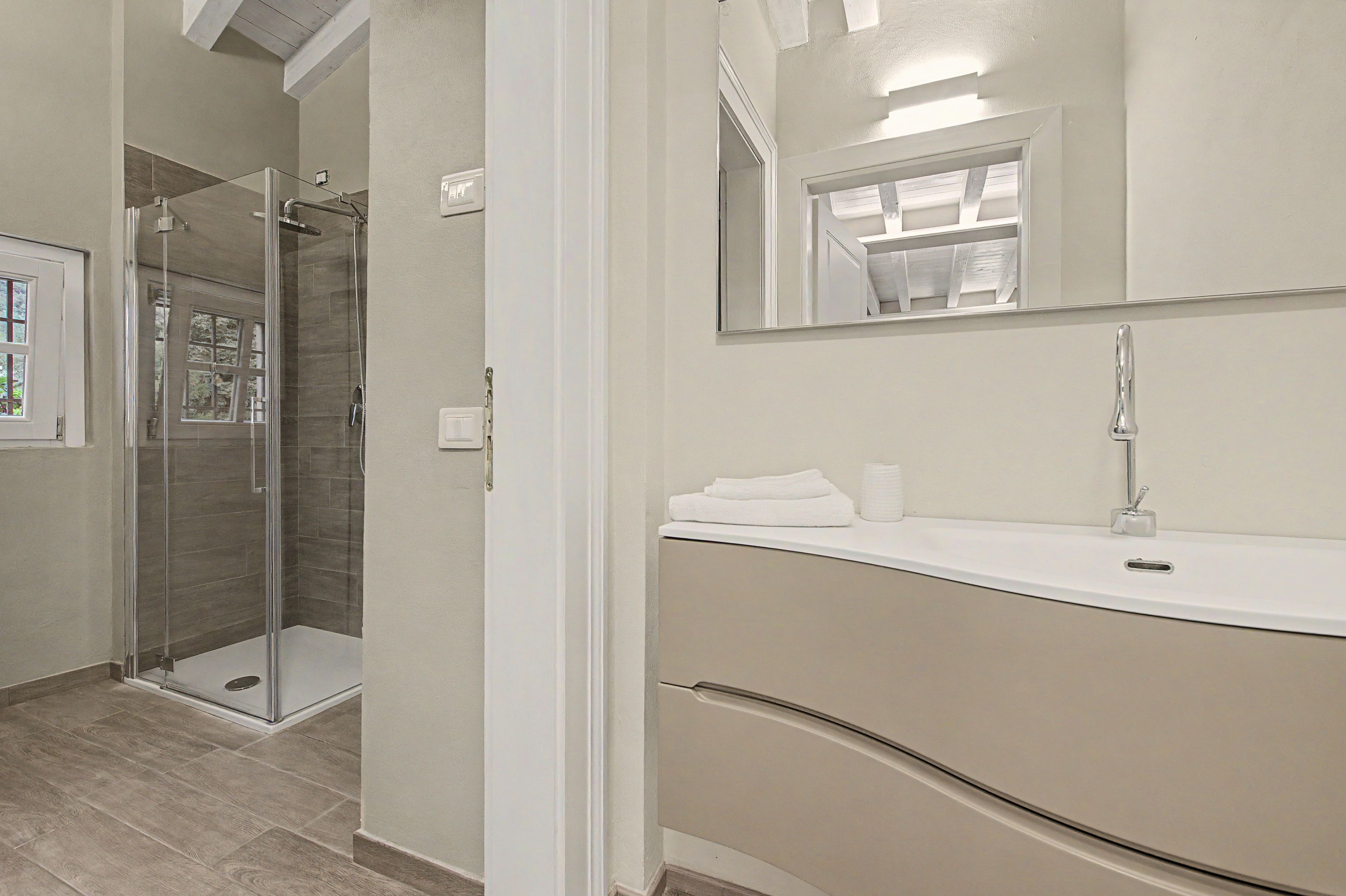 Un baño moderno con cabina de ducha de vidrio, tocador blanco con espejo y armario beige.
