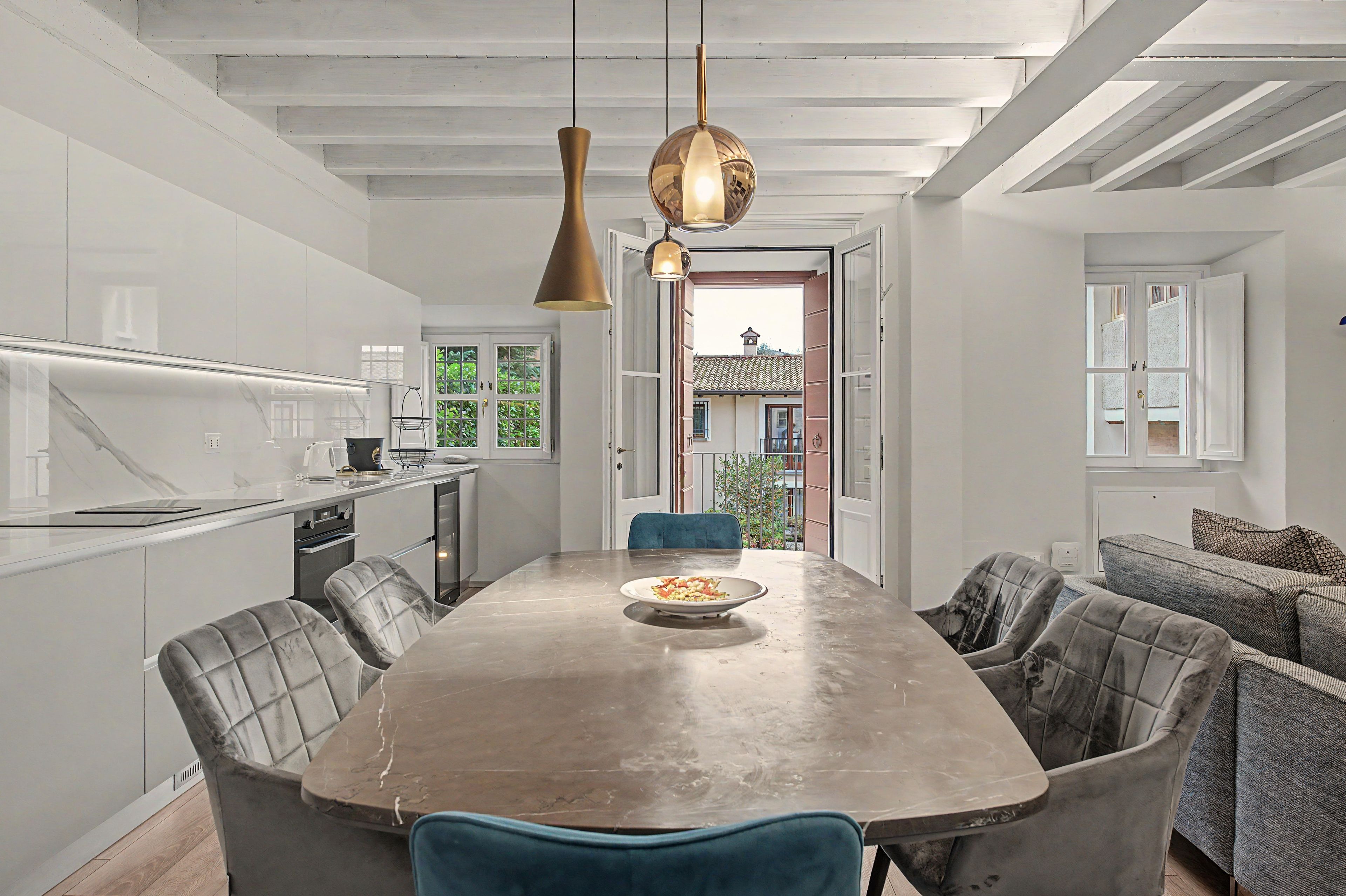 A modern kitchen with a central island, pendant lighting, and a view of a balcony.