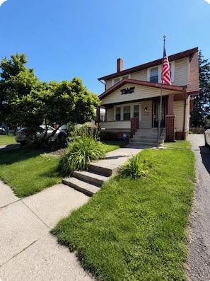 A two-story house with a front porch, a flag, and a mailbox.