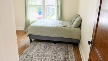 Quarto com cama, ventilador de teto, janela com cortinas e tapete estampado.