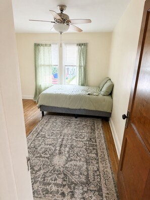 Un dormitorio con cama, ventilador de techo, ventana con cortinas y alfombra estampada.