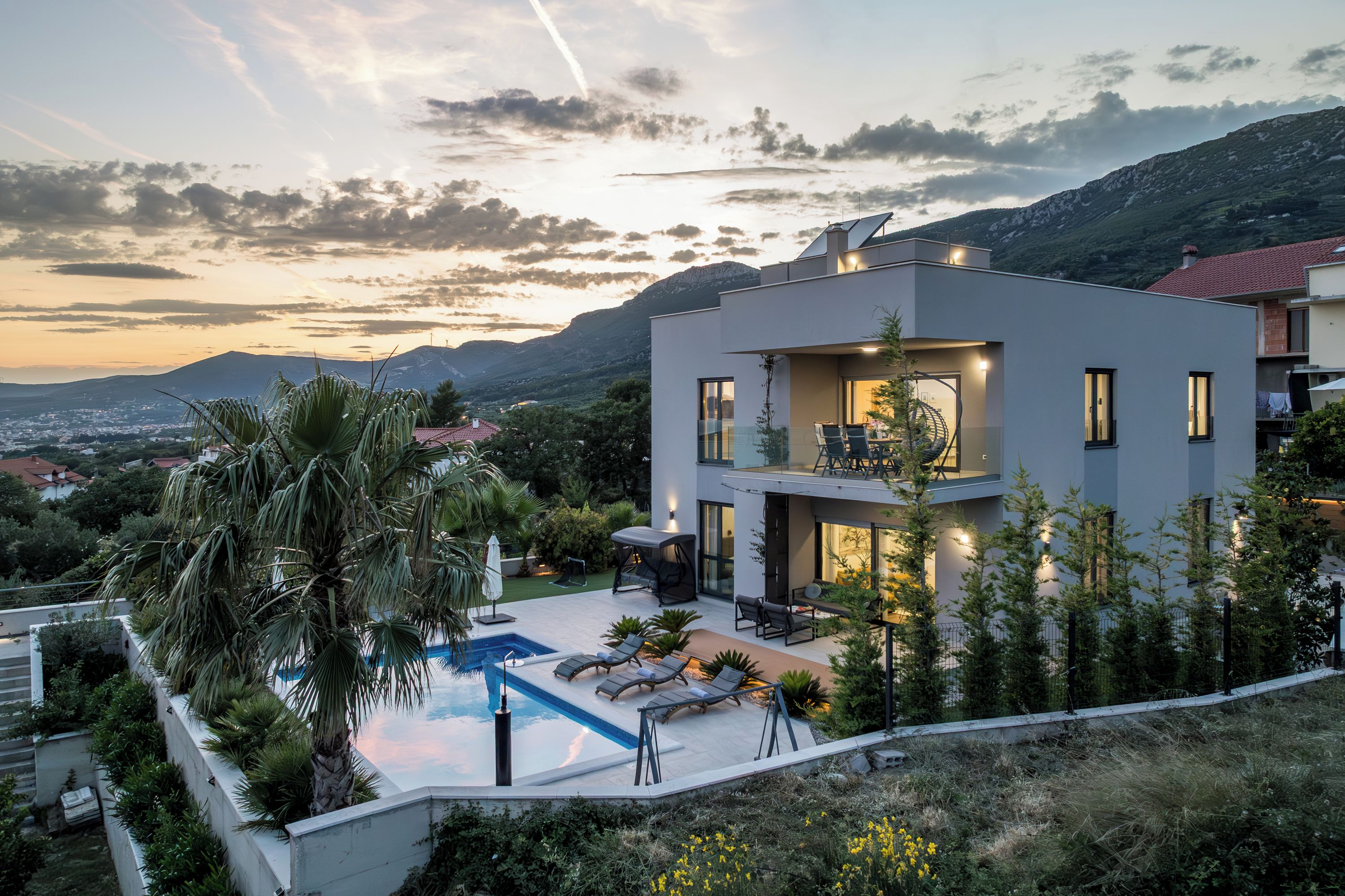 Ein modernes, zweistöckiges Haus mit Swimmingpool, Sitzgelegenheiten im Freien und Blick auf die umliegende Landschaft.