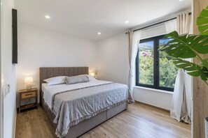 A bedroom with a bed, bedside tables, a window with curtains, and a view of greenery outside. - Villa Belvedere, Sea View with Pool (Kaštel Kambelovac)