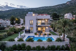 A modern two-story house with a swimming pool, surrounded by lush greenery and a mountainous backdrop. - Villa Belvedere, Sea View with Pool (Kaštel Kambelovac)