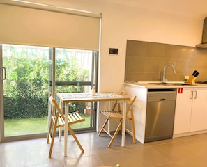 A modern kitchen with a built-in dishwasher, a sink, and a window overlooking a garden. - 42 Easy 2BR Business Stay Parking, Kitchen & Wi-Fi (Coogee)
