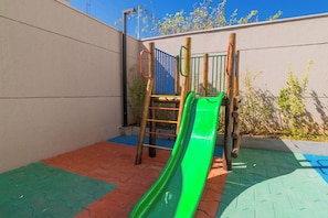 Ein Spielplatz mit einer grünen Rutsche und einer blauen Kletterkonstruktion an einer Wand.