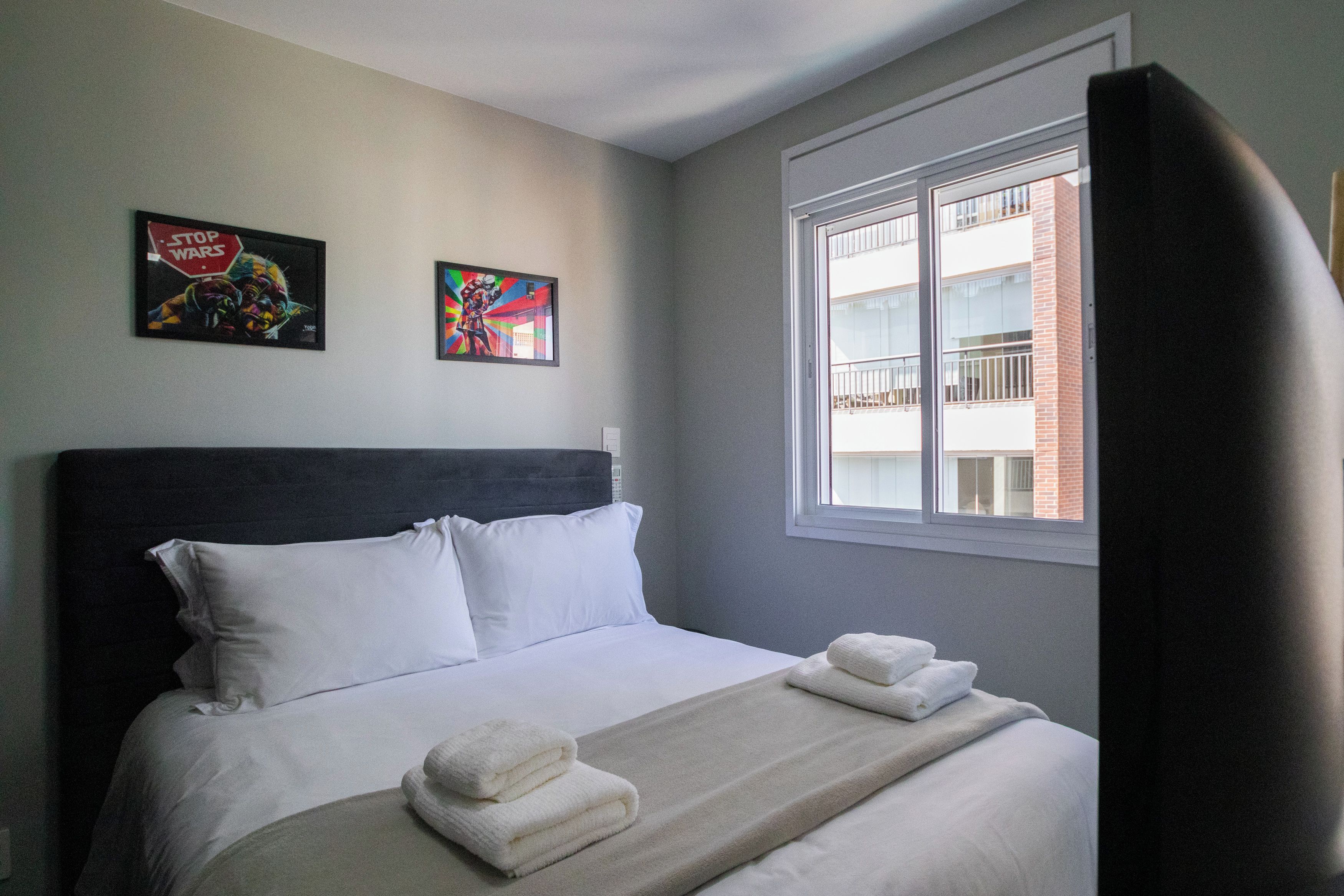 A hotel room with a bed, pillows, a blanket, and two wall art pieces.