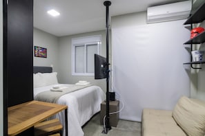 Ein Hotelzimmer mit Bett, Schreibtisch, Stuhl, Fernseher, Klimaanlage und einem Fenster mit Jalousien.