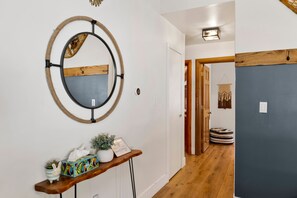 A hallway with a wooden bench, a wall-mounted mirror, and a door leading to another room. - Big Bear Lake 2BR Cabin | Hot Tub, Arcade Game Room, Fire Pit & Covered Deck (Big Bear Lake)