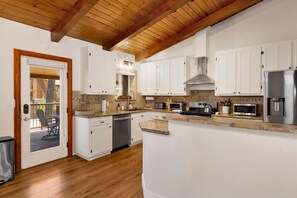 A modern kitchen with white cabinets, a stainless steel refrigerator, and a wooden ceiling. - Big Bear Lake 2BR Cabin | Hot Tub, Arcade Game Room, Fire Pit & Covered Deck (Big Bear Lake)