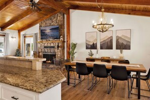 A spacious dining area with a stone fireplace, modern furniture, and a view of the outdoors. - Big Bear Lake 2BR Cabin | Hot Tub, Arcade Game Room, Fire Pit & Covered Deck (Big Bear Lake)