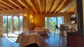 A cozy cabin with a wooden interior, a sofa, a table with a kettle, and a view of the outdoors.