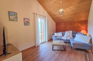 Een gezellige woonkamer met een houten plafond, een zithoek, een salontafel en een televisie.