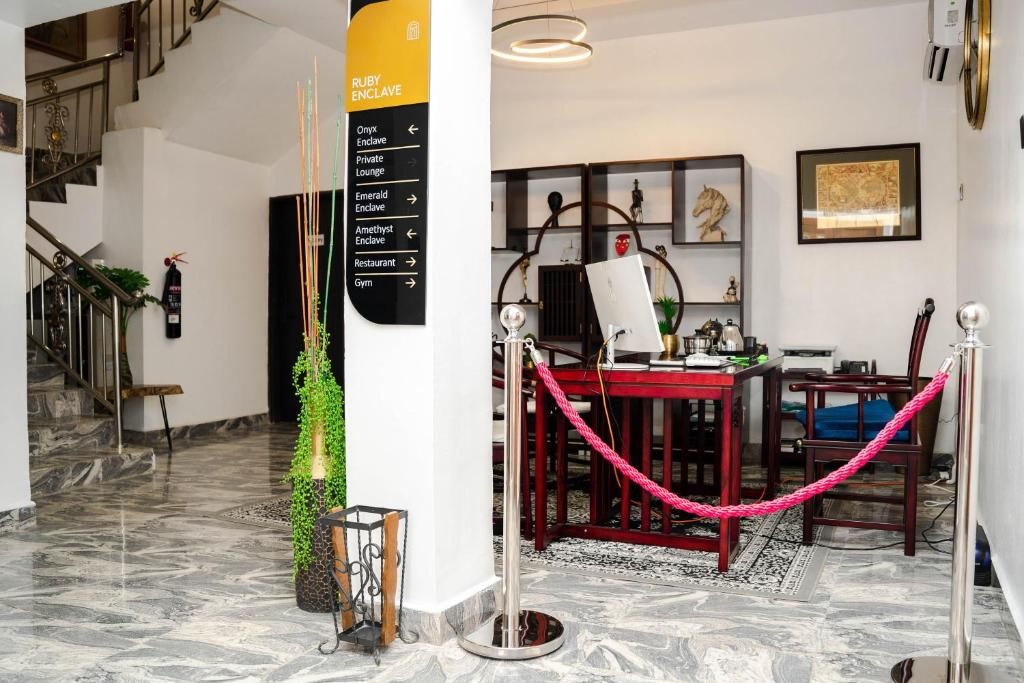 A lobby with a marble floor, a staircase, a red table with chairs, a pink rope barrier, and a sign listing amenities like a gym and restaurant.