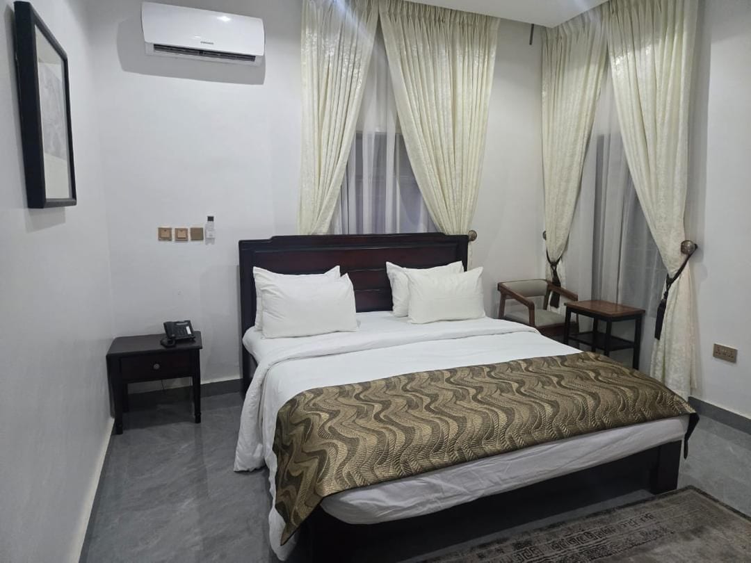 A hotel room with a bed, bedside tables, an air conditioner, and curtains.