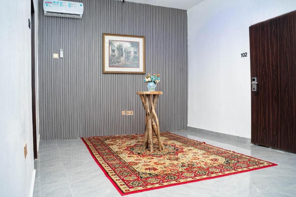 Un pasillo con pared gris, un cuadro enmarcado, una pequeña mesa de madera con un jarrón y un tapete rojo estampado.