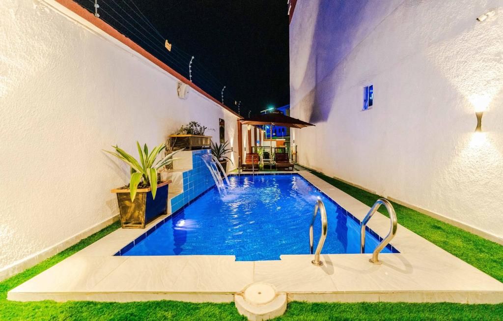 Una piscina con fuente, rodeada por un muro blanco y un pequeño jardín con plantas.