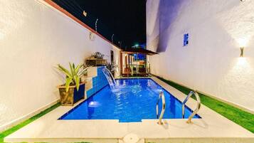 Una piscina con fuente, rodeada por un muro blanco y un pequeño jardín con plantas.