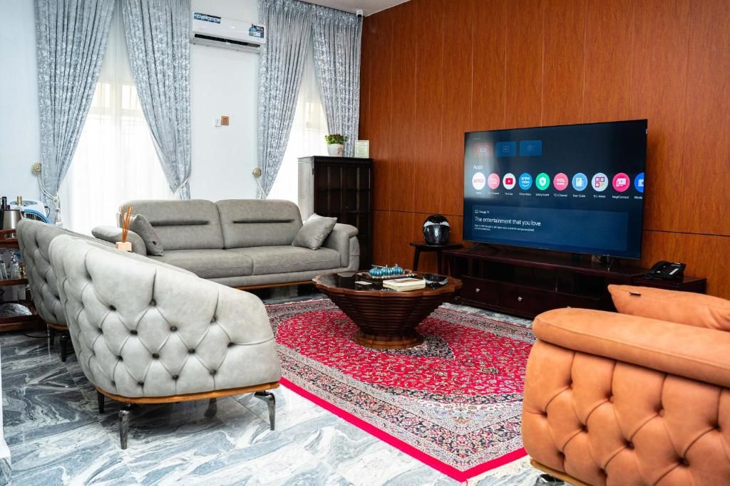 Una sala de estar con sofá, sillón, reposapiés, mesa de centro y televisor de pantalla plana.