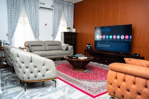 Ein Wohnzimmer mit Sofa, Sessel, Hocker, Couchtisch und Flachbildfernseher.