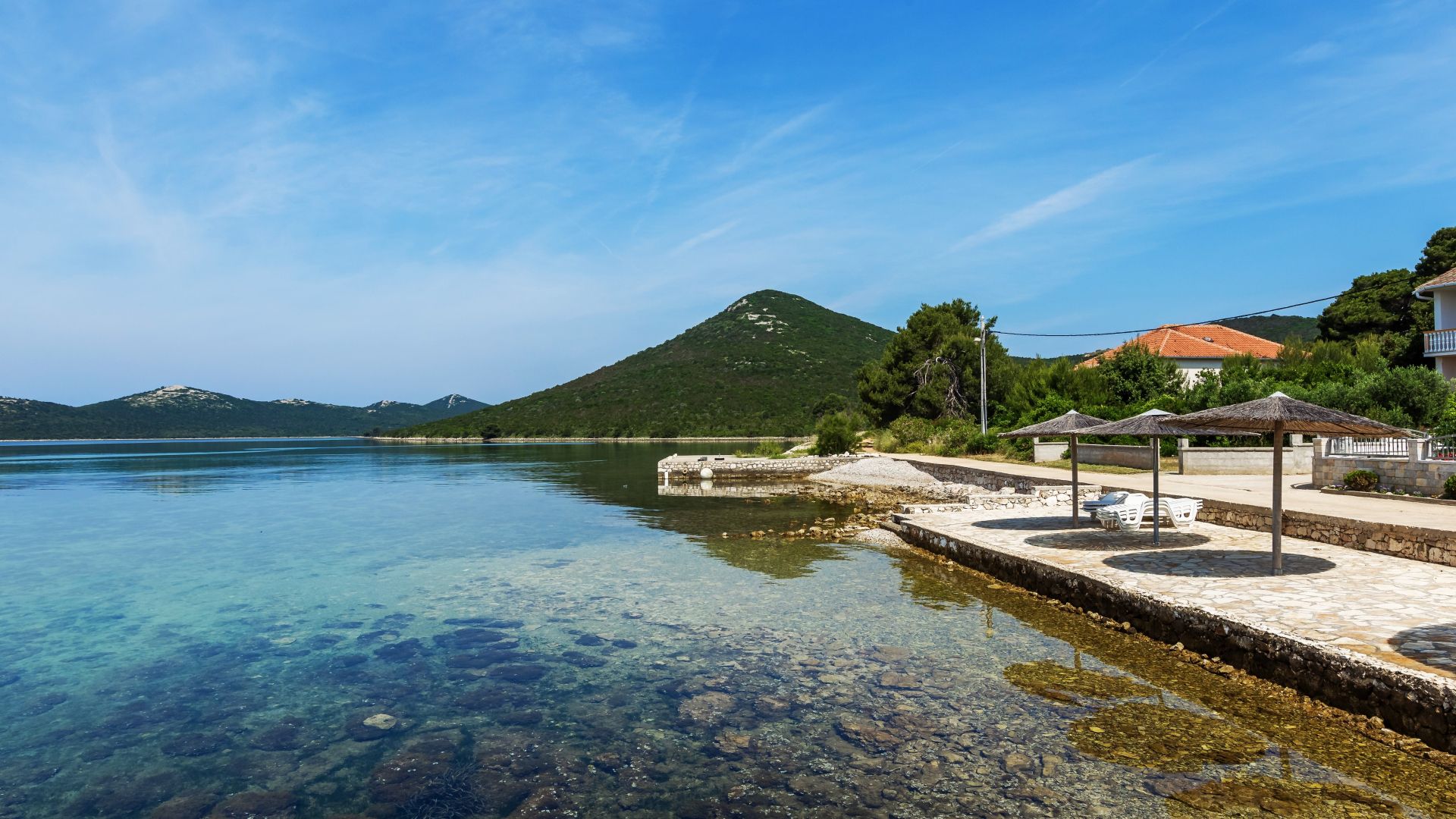 Eine Küstenlandschaft mit klarem Wasser, einem Steg und einem Berg im Hintergrund.